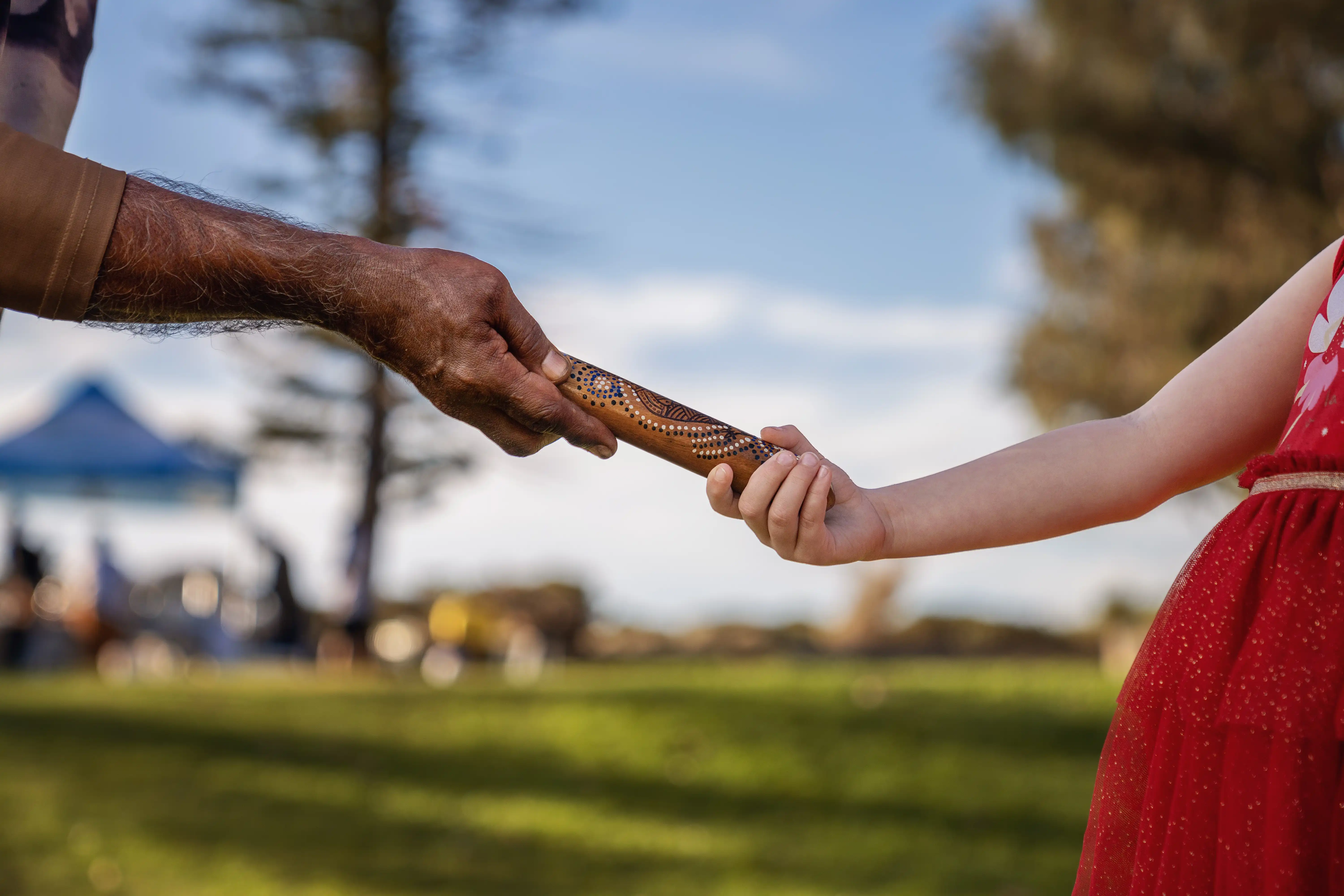 Close-up of two people holding a decorated wooden object outdoors.