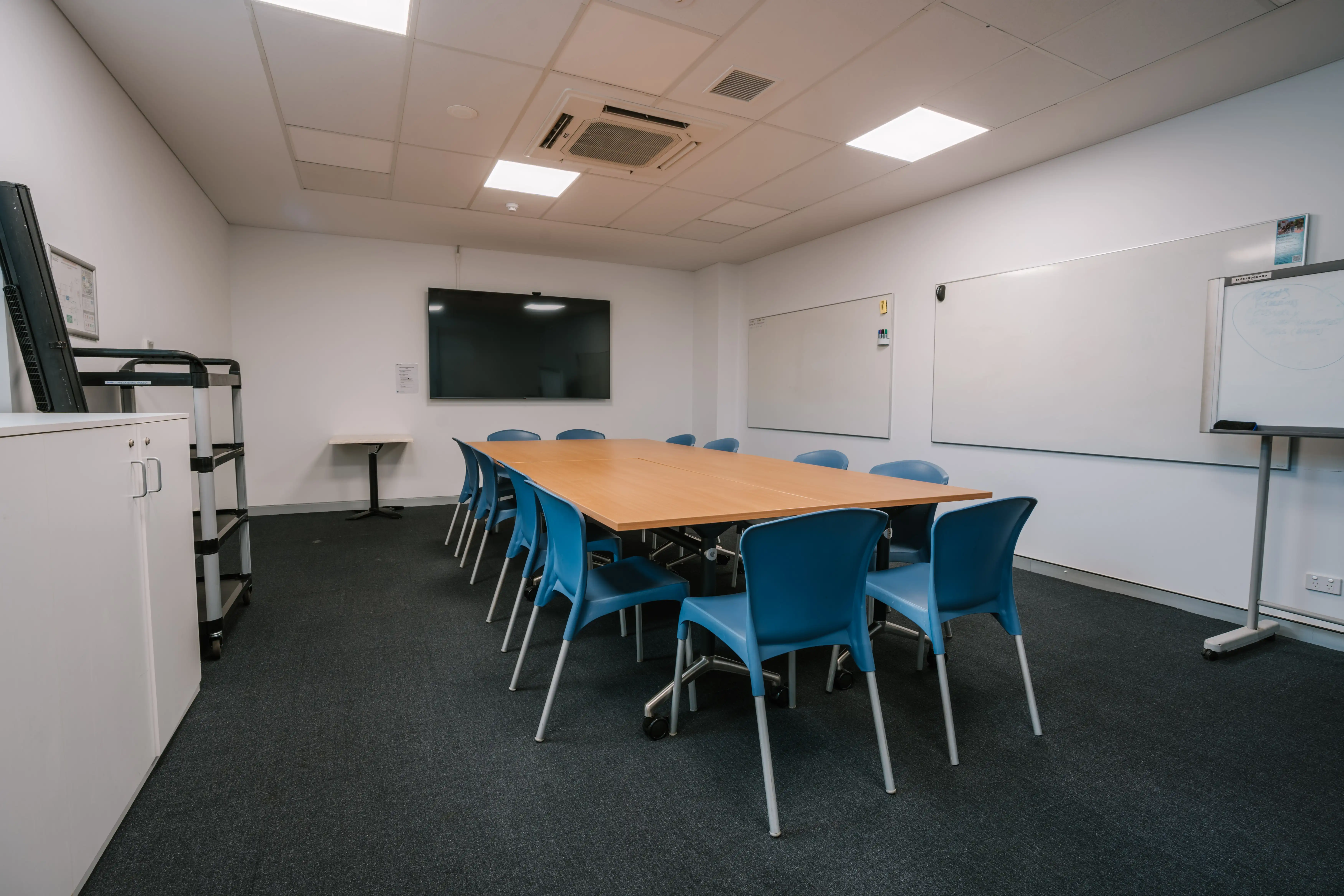 MARC multi purpose room with 12 chairs around a table, whiteboards and a TV screen
