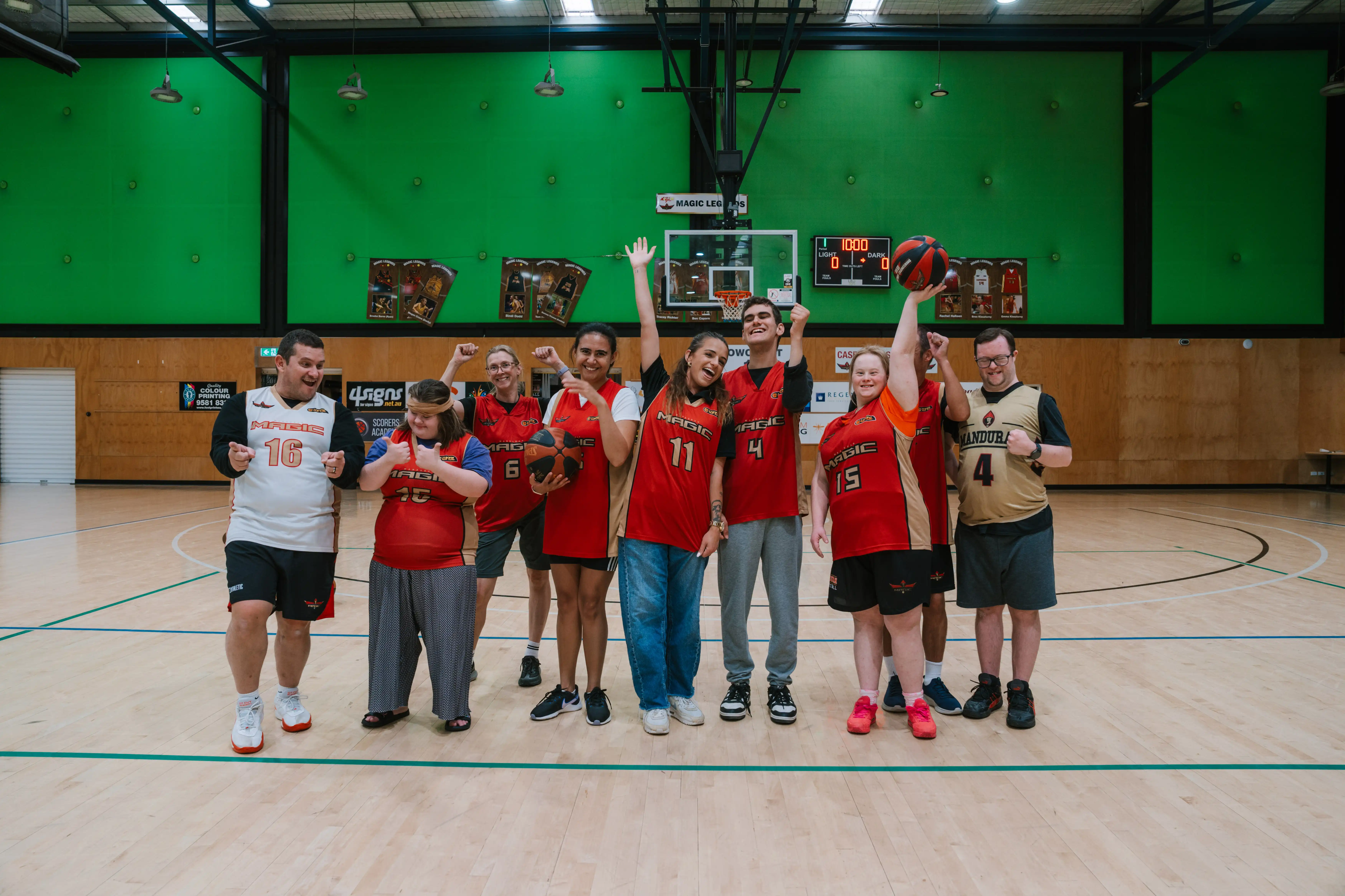 Inclusive basketball team celebrating together on an indoor court, with players holding a ball and raising their arms.