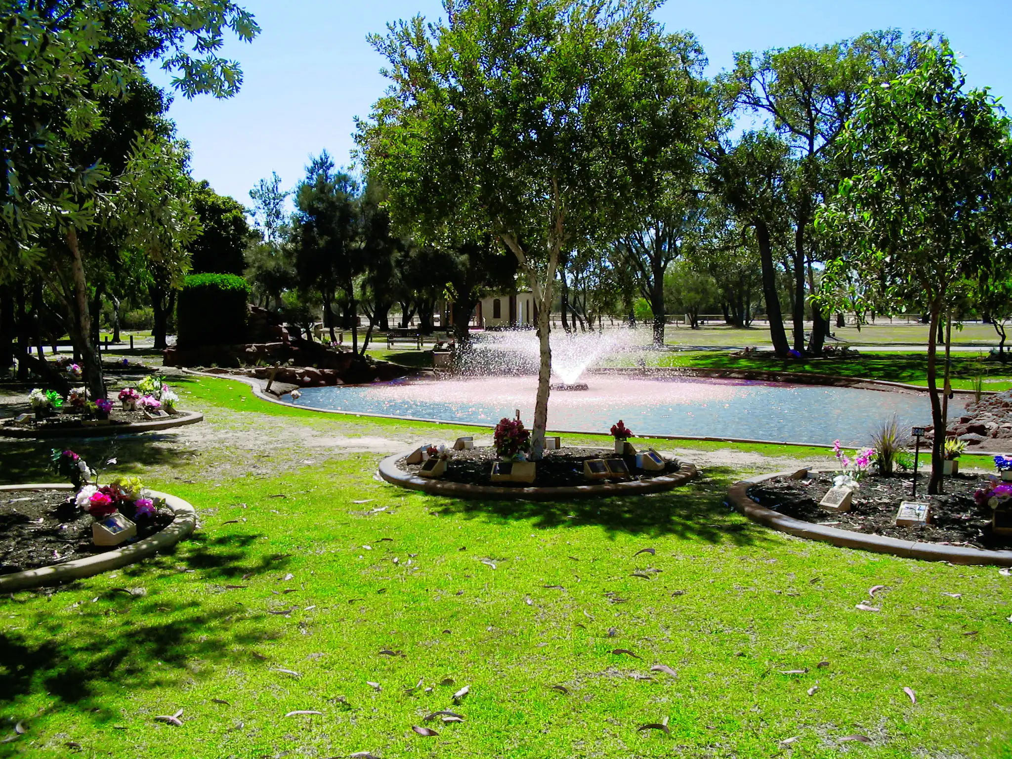 A lawn cemetery with circular garden beds and a pond with a fountain among trees