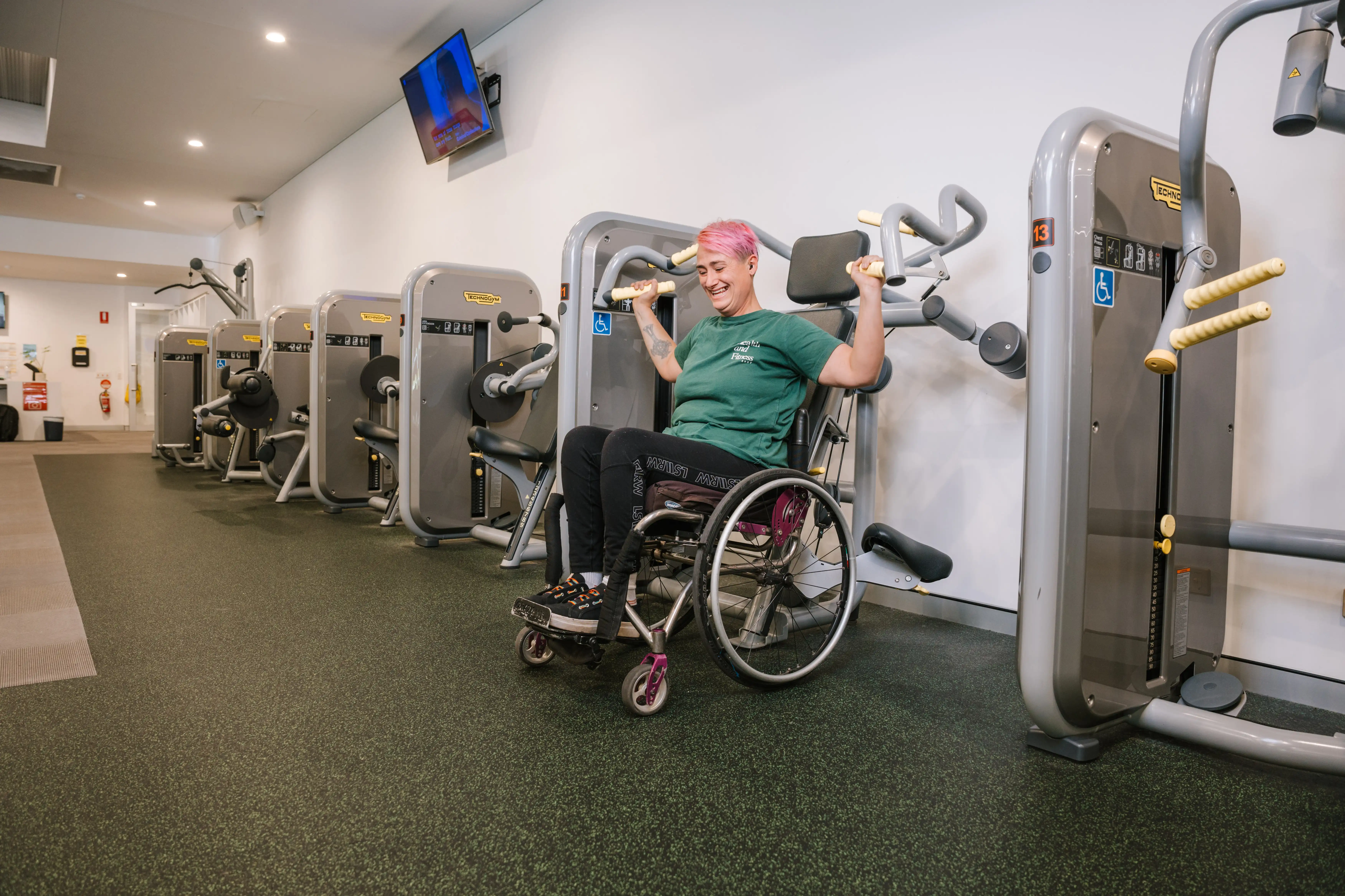 Person using an upper‑body exercise machine while seated in a wheelchair at a gym.
