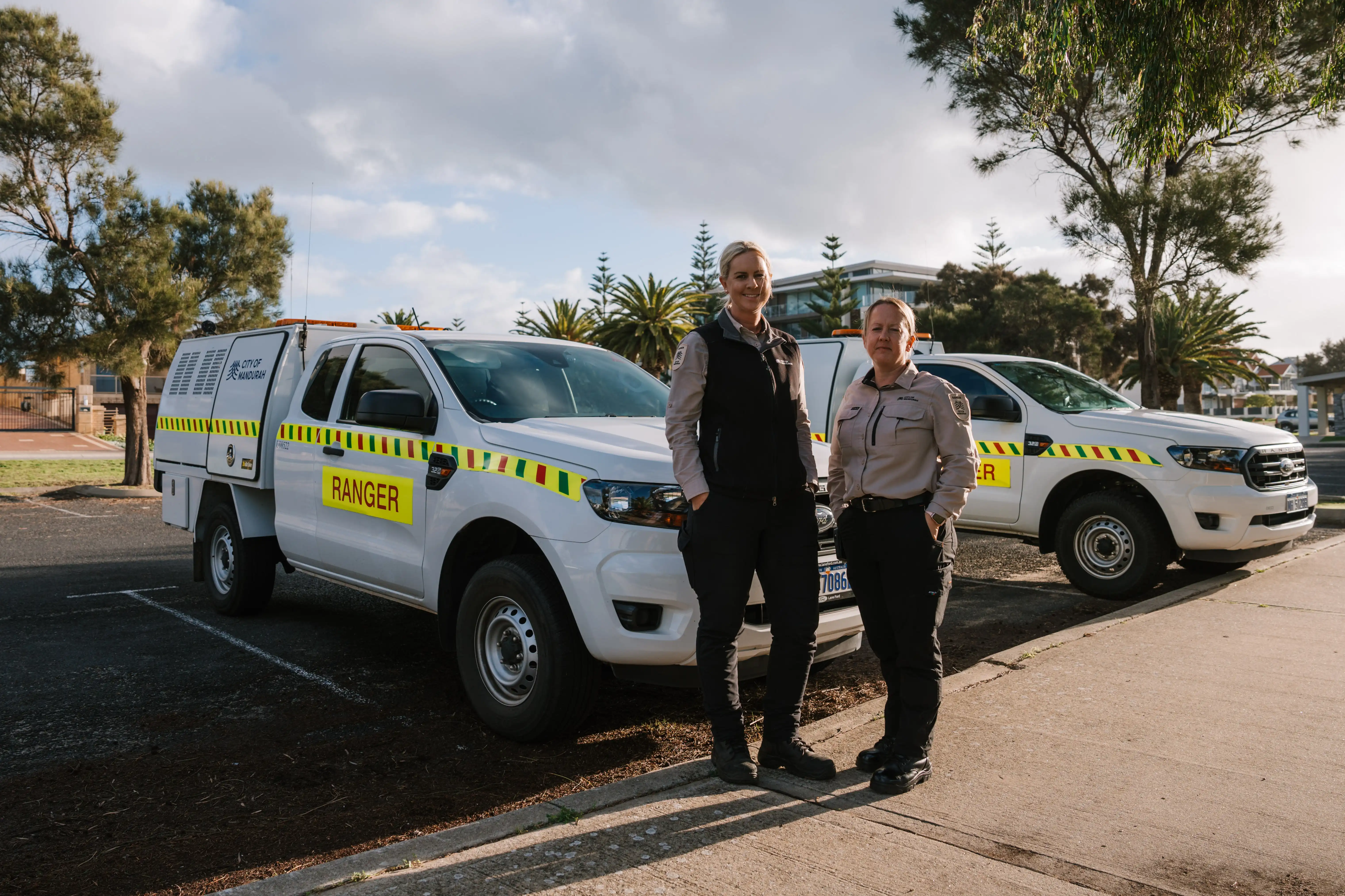 Two uniformed rangers standing beside white ranger vehicles parked outdoors