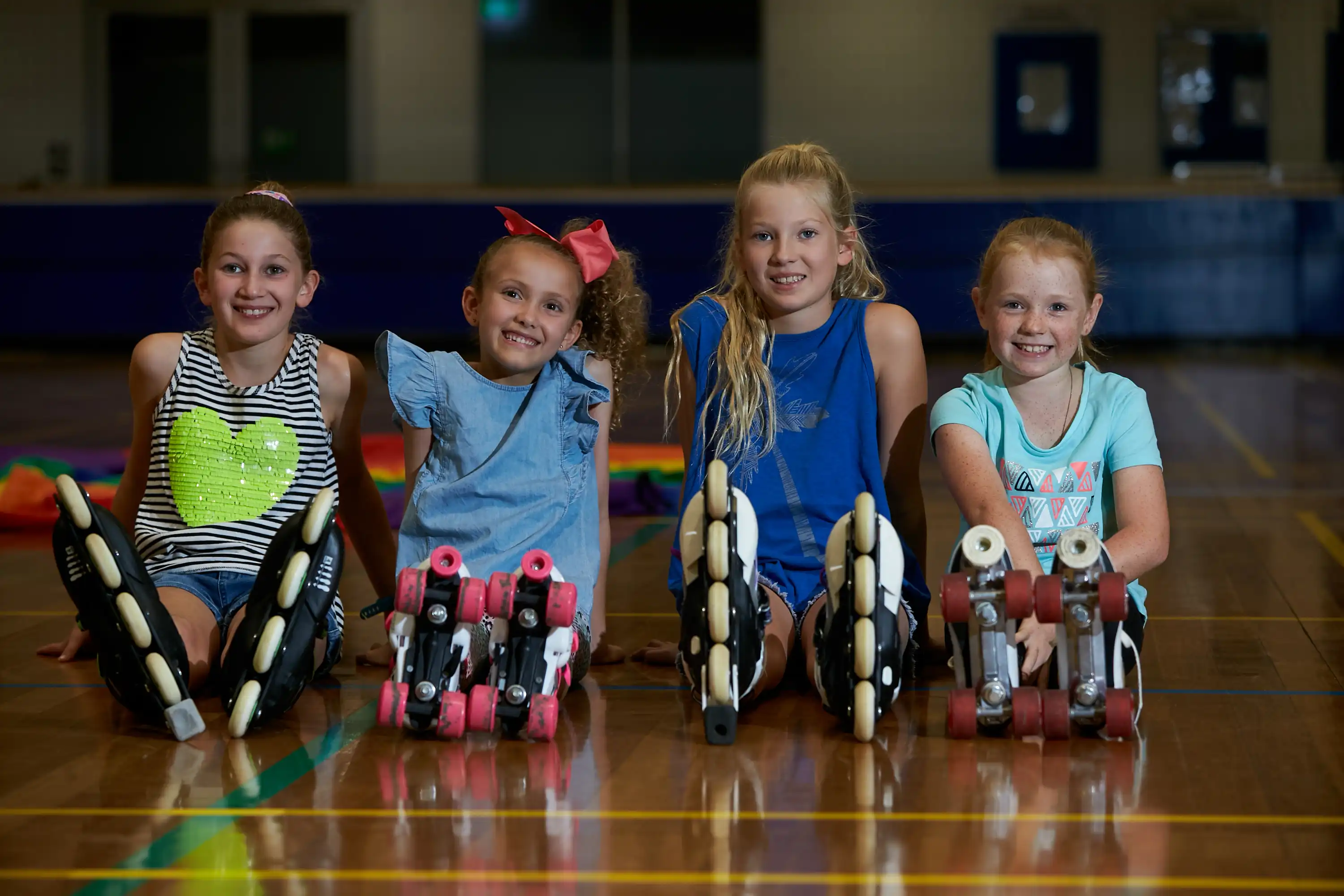 Four young people sitting down with roller blades on in gym.