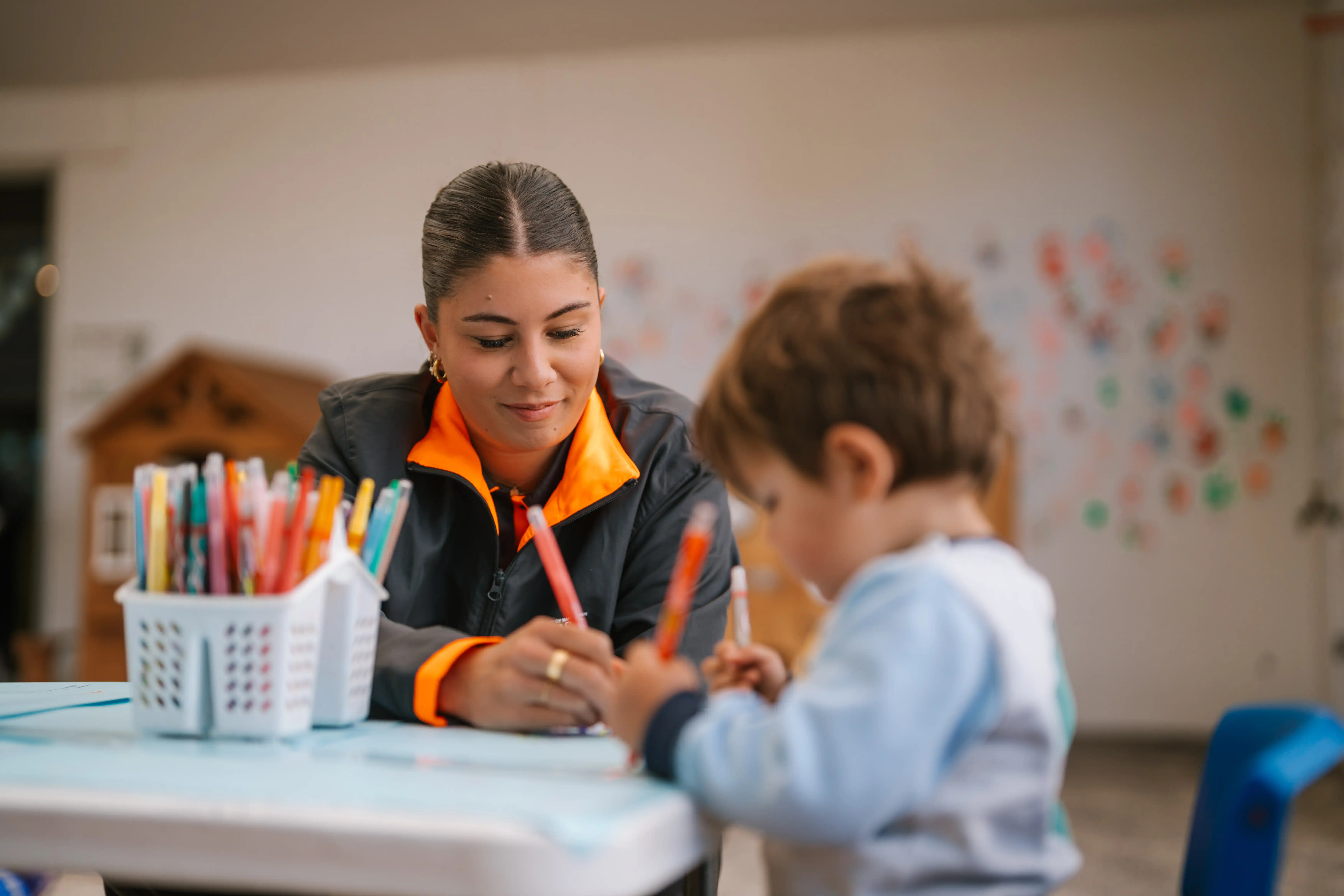 Carer helping a young child draw at a table in the MARC crèche