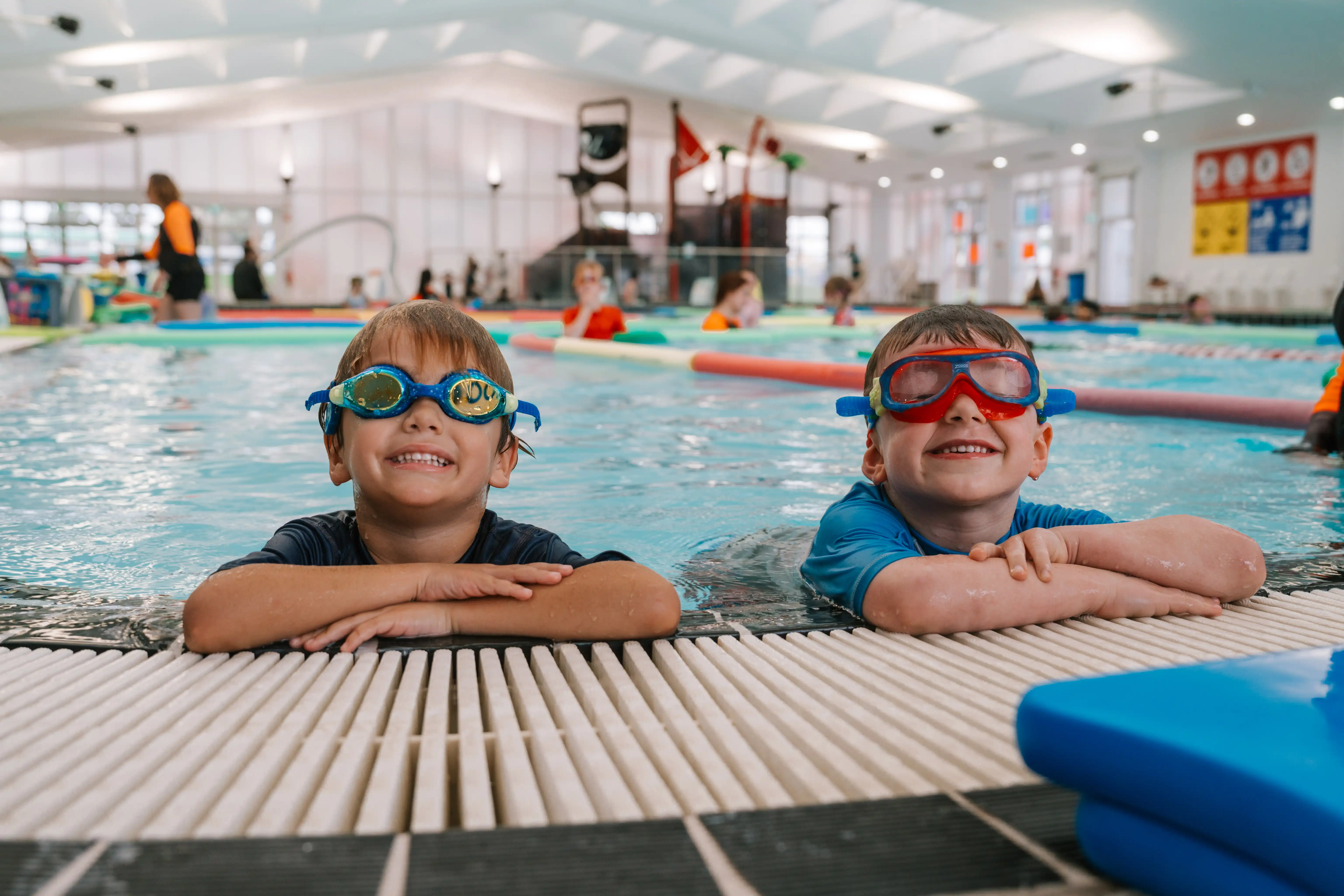 Two children smiling at the edge of an indoor swimming pool at MARC